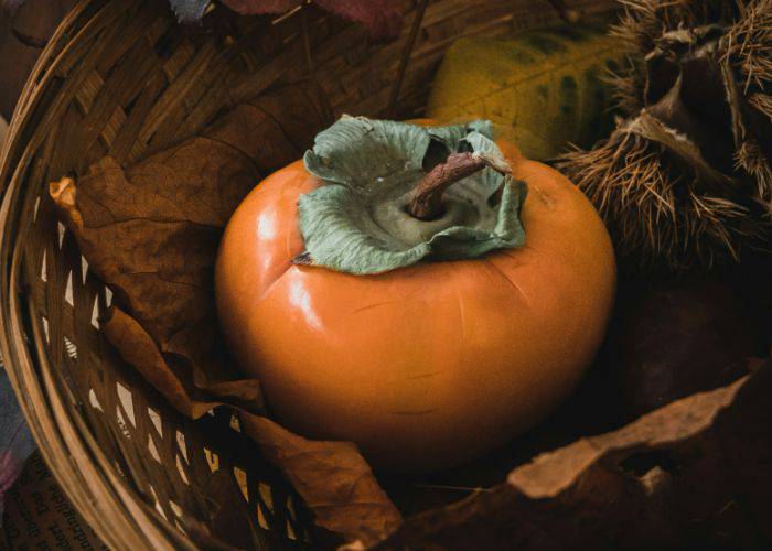 Kaki persimmon in a wicker basket, nestled into fall foliage.